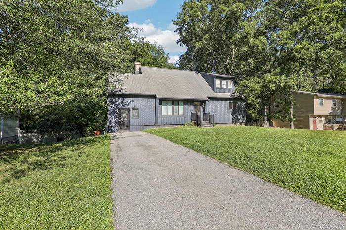 View of front of home featuring a front lawn, driveway, a shingled roof, and a chimney