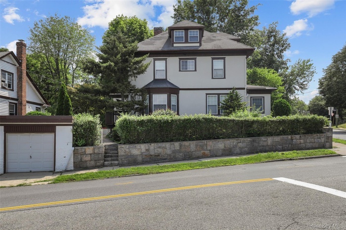 View of front of home featuring stucco siding, a chimney, an outdoor structure, and concrete driveway