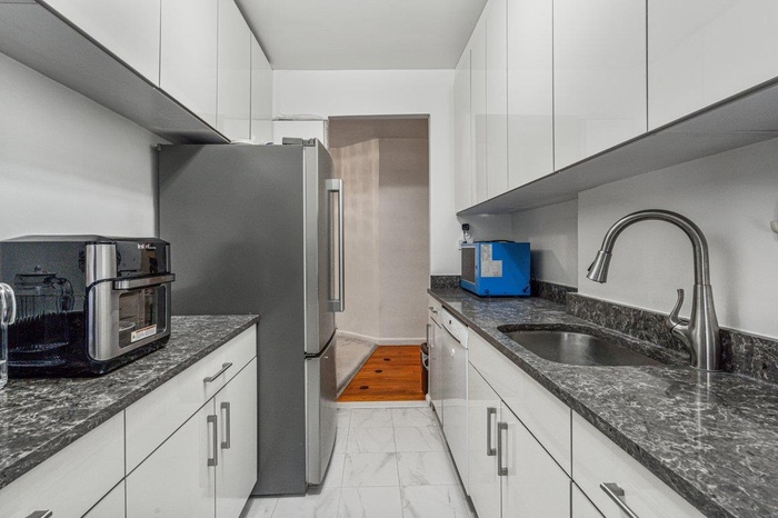Kitchen with dark stone counters, a sink, marble finish floor, white cabinets, and freestanding refrigerator