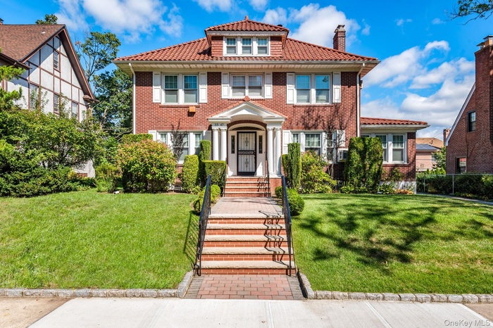 View of front of house featuring a chimney, a front lawn, brick siding, and a tiled roof