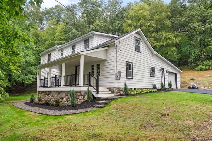 View of front of house featuring covered porch, a front yard, driveway, and an attached garage