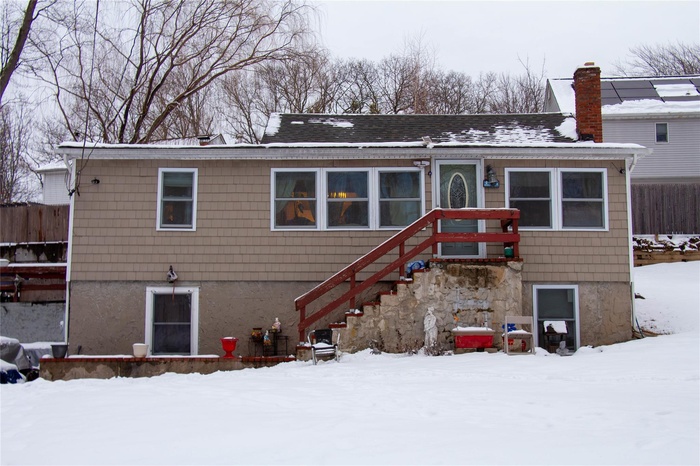 Snow covered back of property with stairs, fence, roof with shingles, and a chimney