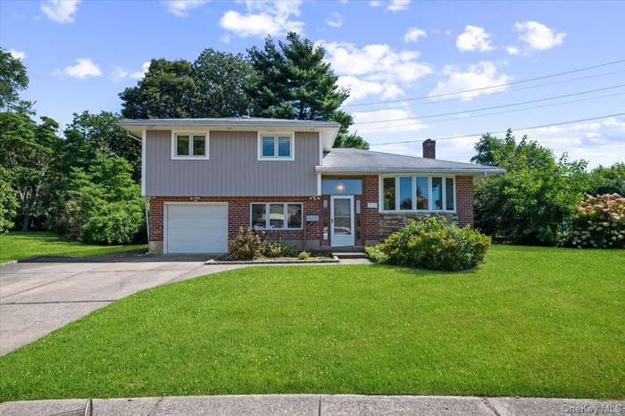 Tri-level home with brick siding, a garage, and a front lawn
