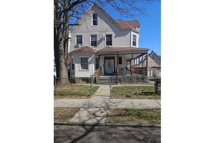 View of front facade featuring a porch, stucco siding, and a fenced front yard