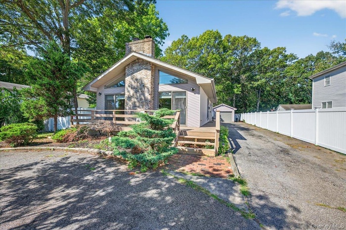 View of front of house featuring an outbuilding, a deck, a chimney, a detached garage, and view of scattered trees