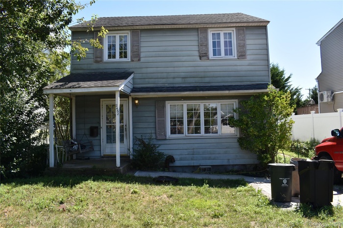 View of front facade with roof with shingles, a front yard, and covered porch
