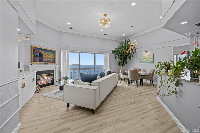 Living room featuring ornamental molding, a water view, light wood finished floors, a glass covered fireplace, and recessed lighting