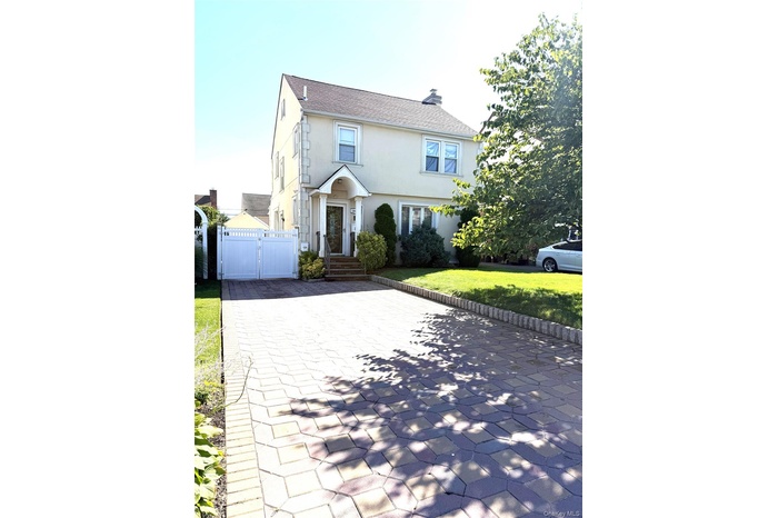 Colonial-style house with a gate, a shingled roof, stucco siding, a chimney, and a front lawn