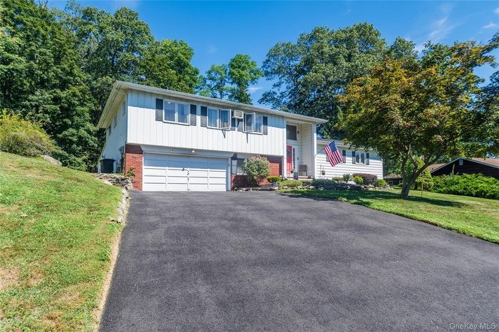 Raised ranch featuring brick siding, driveway, an attached garage, and a front lawn