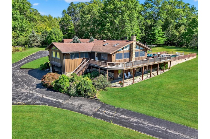 Back of house with asphalt driveway, stairway, a chimney, a yard, and a shingled roof
