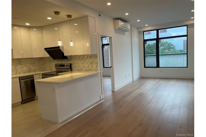 Kitchen with modern cabinets, white cabinets, stainless steel appliances, light wood finished floors, and recessed lighting