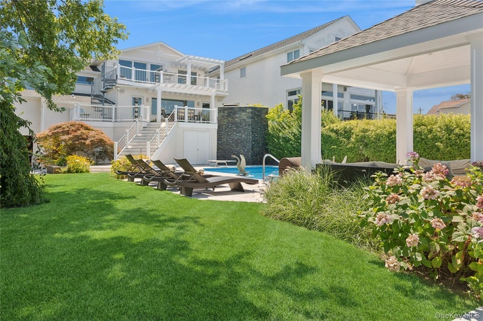 Rear view of property featuring stairs, a patio area, a lawn, a balcony, and an outdoor pool