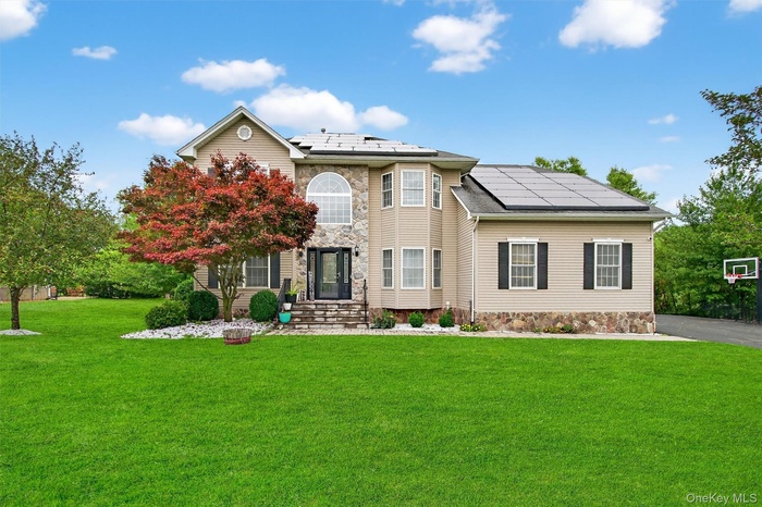View of front facade with roof mounted solar panels, a front yard, and stone siding