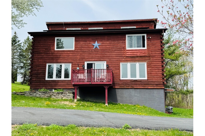 View of log home with a deck as you pull into the driveway.