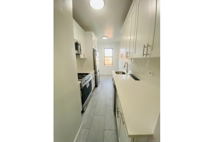 Kitchen with white cabinets, appliances with stainless steel finishes, backsplash, light tile patterned flooring, and light stone counters