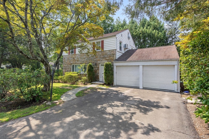 View of front of house with stone siding, an attached garage, driveway, and a shingled roof