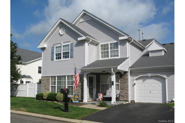 Traditional-style home with stone siding, a garage, driveway, roof with shingles, and a porch