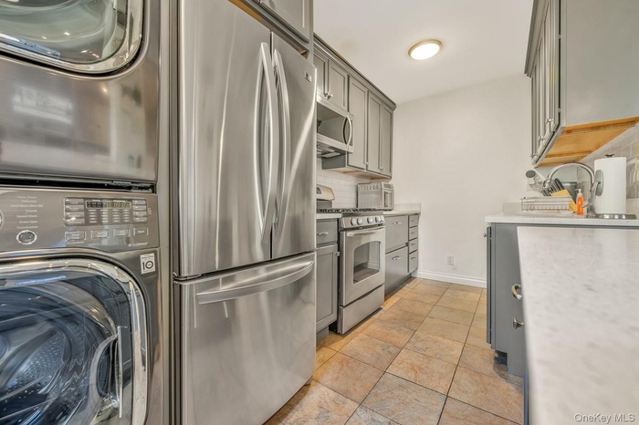 Kitchen with gray cabinets, appliances with stainless steel finishes, stacked washer and clothes dryer, and backsplash