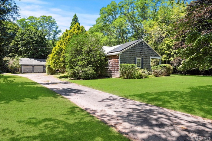 View of front facade with an outdoor structure, a front yard, view of scattered trees, and solar panels