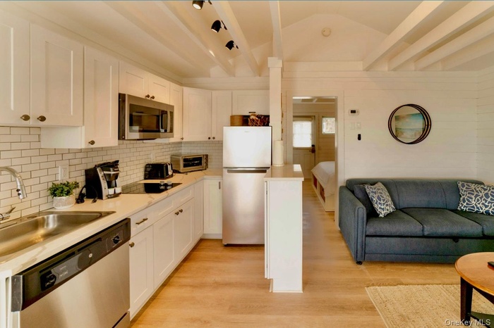 Kitchen featuring appliances with stainless steel finishes, light countertops, light wood-type flooring, tasteful backsplash, and white cabinets