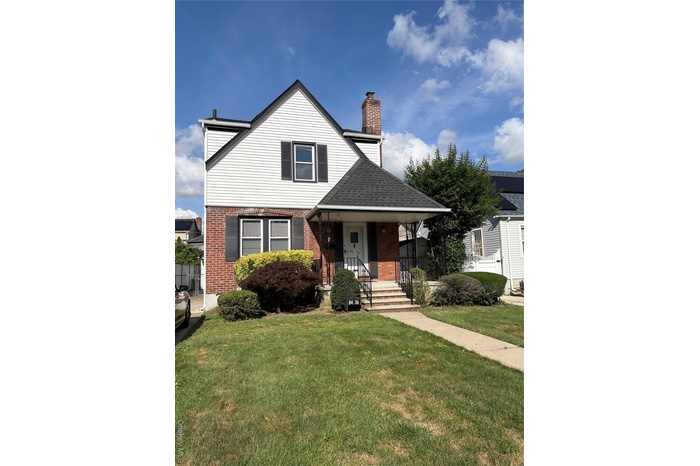 View of front of house with brick siding, a front yard, a chimney, roof with shingles, and a porch