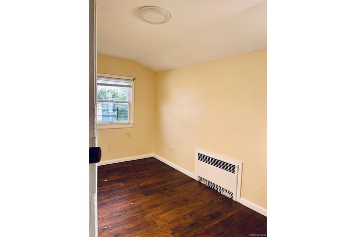 Spare room featuring dark wood-style flooring and radiator heating unit