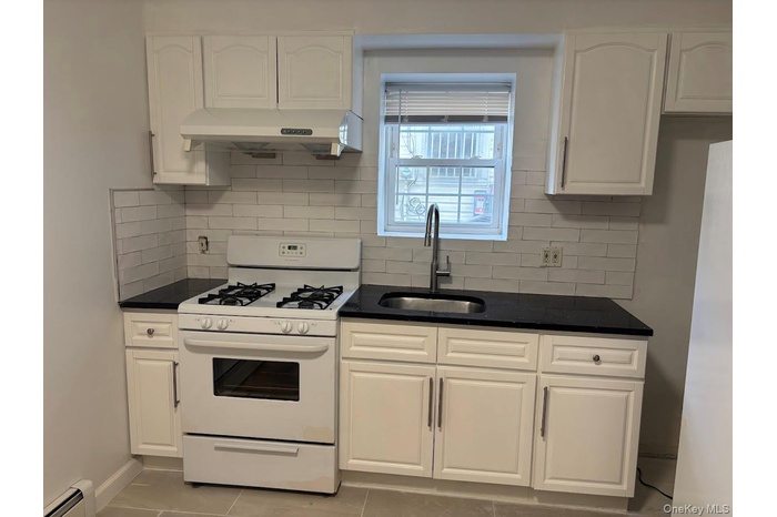 Kitchen featuring gas range gas stove, backsplash, white cabinets, and under cabinet range hood