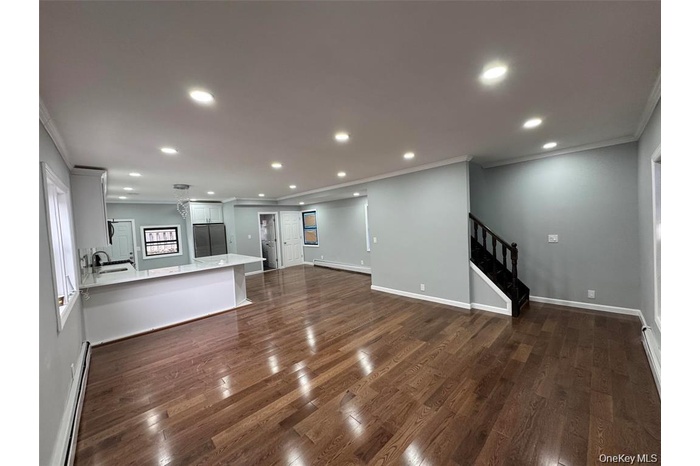 Unfurnished living room featuring crown molding, a baseboard heating unit, stairs, dark wood-style floors, and recessed lighting