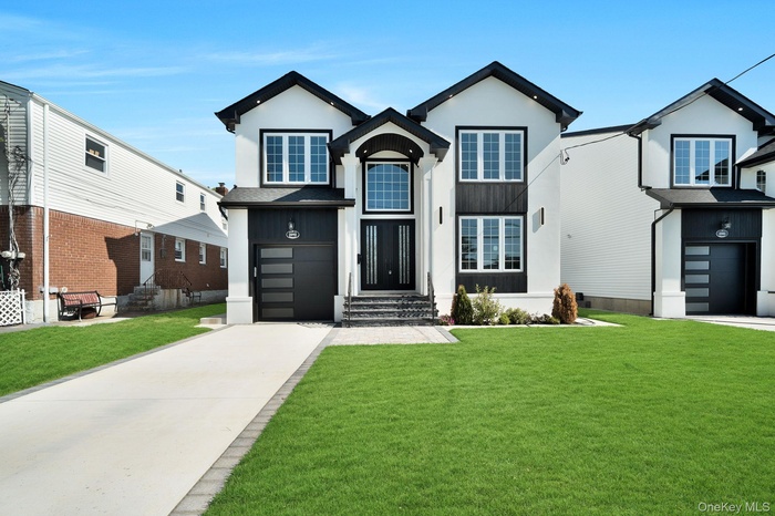 Traditional-style house featuring an attached garage, driveway, a front lawn, and stucco siding