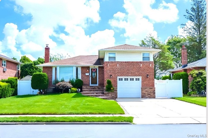 Tri-level home featuring an attached garage, driveway, a gate, and a chimney
