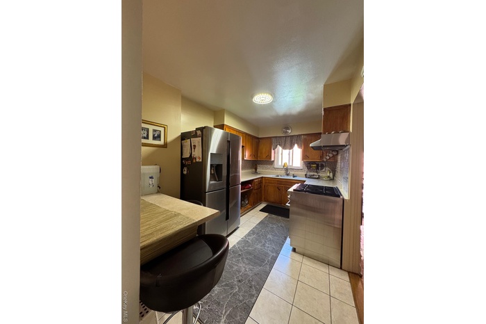 Kitchen with fridge, ventilation hood, backsplash, brown cabinetry, and light tile patterned floors