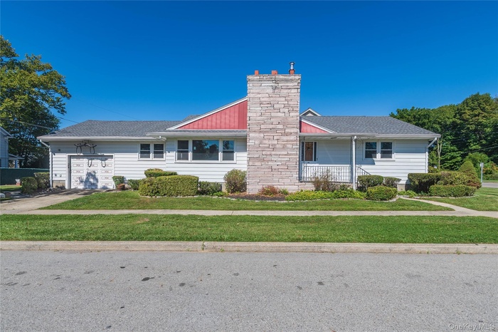 View of front of home with an attached garage, a porch, a chimney, a front yard, and driveway