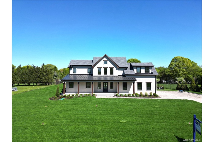 Modern inspired farmhouse featuring a standing seam roof, a porch, a metal roof, a shingled roof, and stucco siding