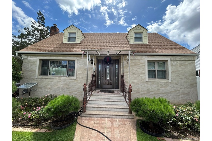 View of front of home with stone siding, a shingled roof, and a chimney
