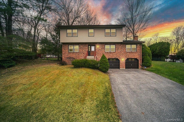 View of front facade with a chimney, driveway, an attached garage, a yard, and brick siding