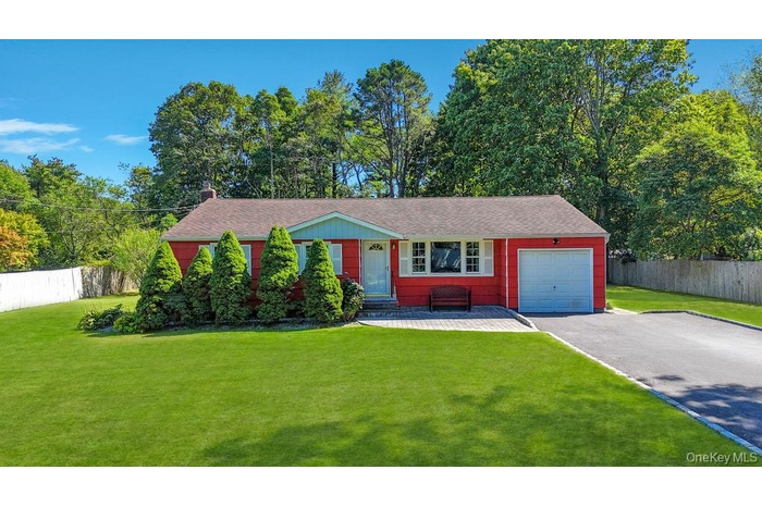 Ranch-style home featuring an attached garage, driveway, a shingled roof, and view of scattered trees