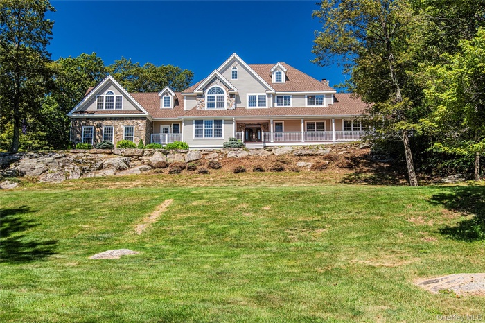 View of front of property with a porch, a front yard, and stone siding