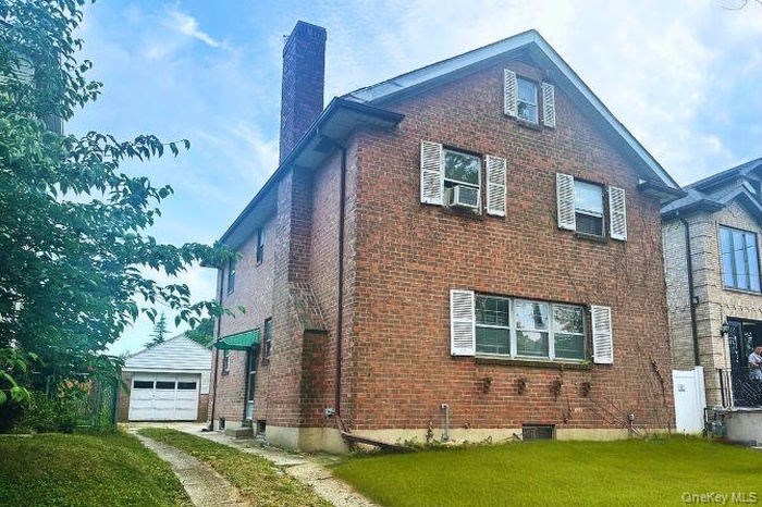 View of property exterior featuring driveway, a chimney, brick siding, a yard, and a garage