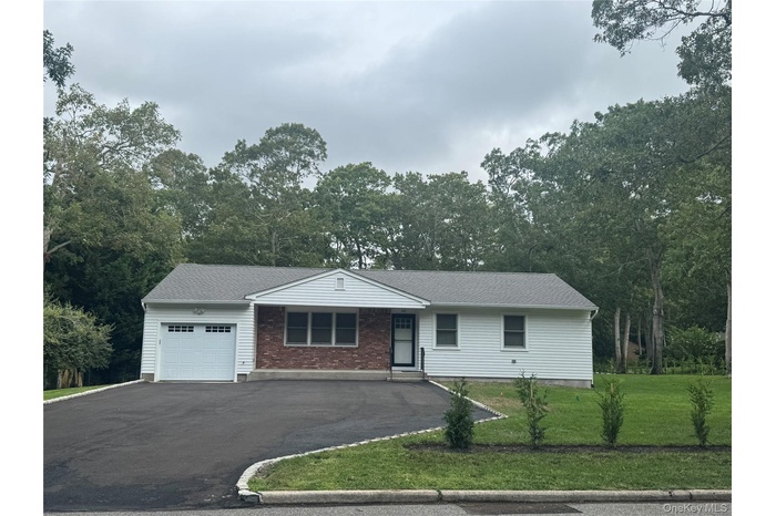 Single story home featuring a garage, driveway, a front yard, and roof with shingles