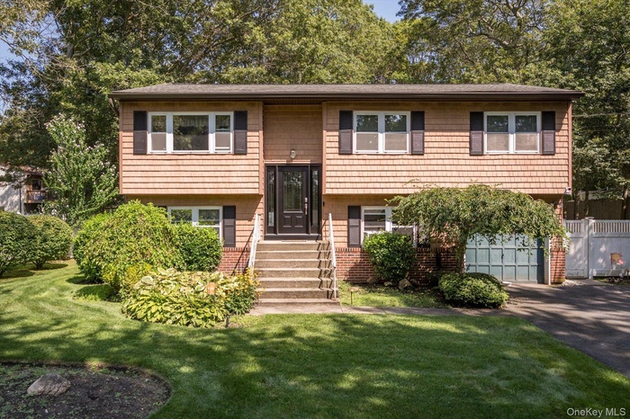 Split foyer home with an attached garage, asphalt driveway, brick siding, and a front yard
