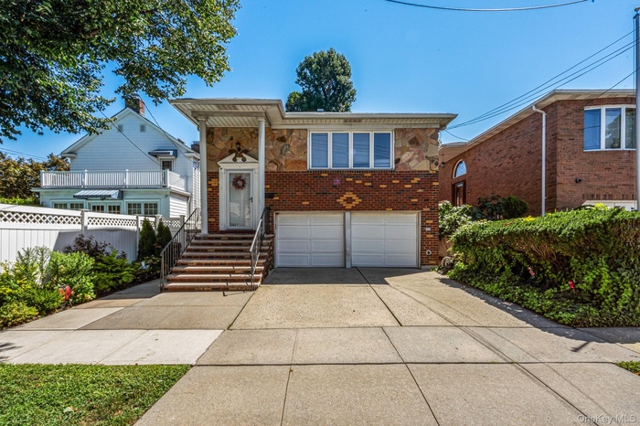 Raised ranch with an attached garage, driveway, stone siding, and brick siding