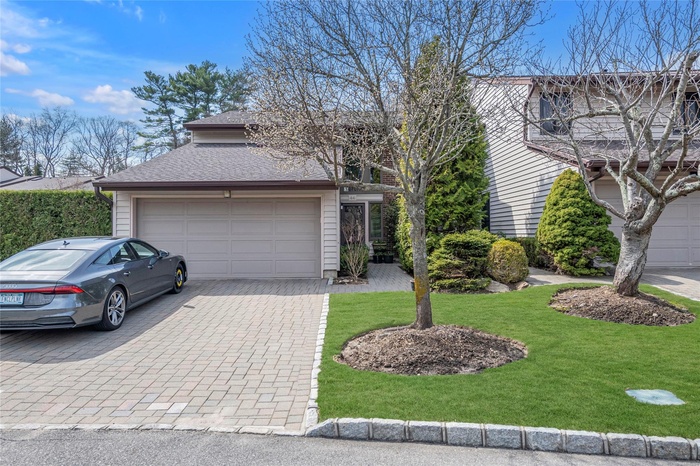 Traditional-style house featuring decorative driveway, a garage, roof with shingles, and a front lawn