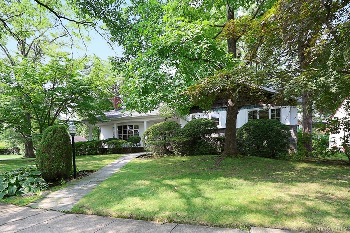 View of property hidden behind natural elements with covered porch and a front yard