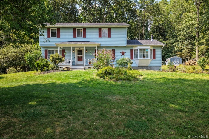 View of front of house featuring covered porch, a front yard, and a storage unit