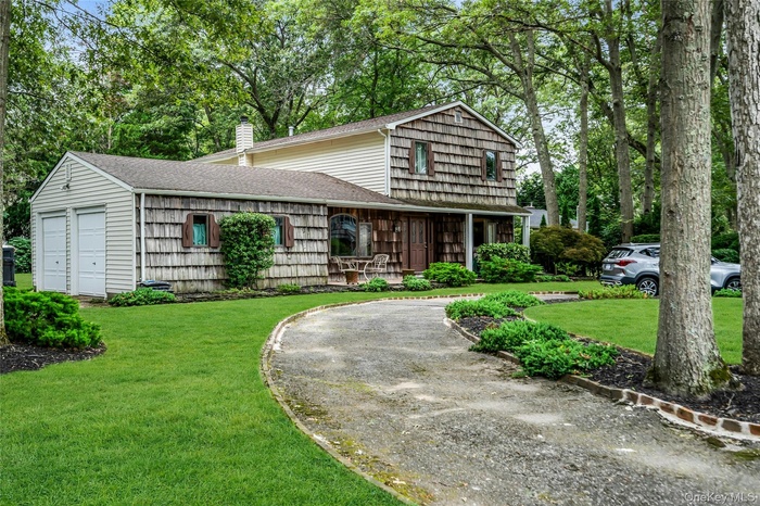 View of front of house with a shingled roof, a front lawn, a chimney, and driveway