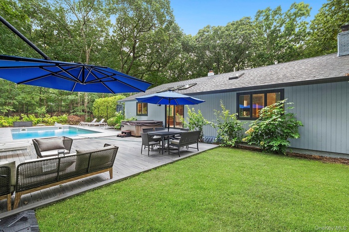 View of grassy yard with a hot tub, a wooden deck, view of scattered trees, and an outdoor pool
