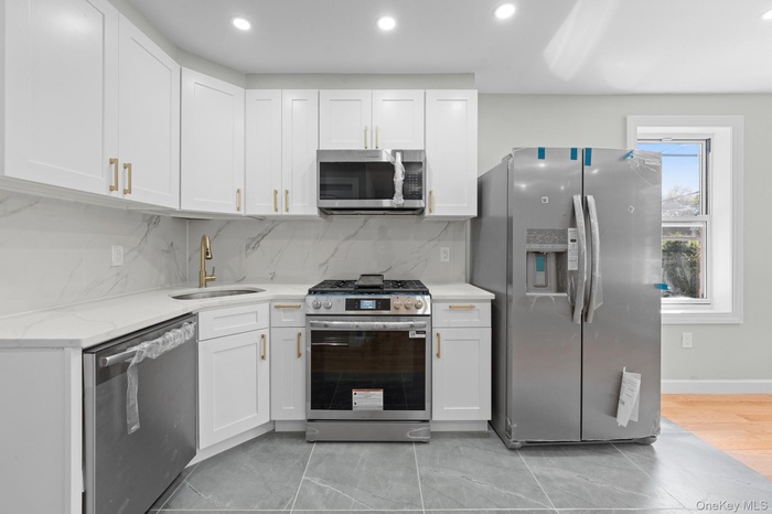 Kitchen featuring decorative backsplash, appliances with stainless steel finishes, white cabinetry, recessed lighting, and light stone countertops