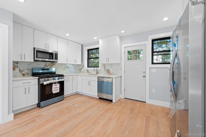 Kitchen with appliances with stainless steel finishes, recessed lighting, backsplash, white cabinetry, and light wood-type flooring