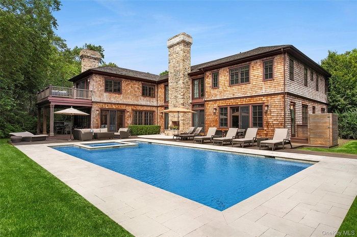 Back of property featuring a patio, a chimney, a pool with connected hot tub, and an outdoor living space