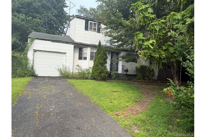 Traditional home with a garage, asphalt driveway, roof with shingles, and a front lawn